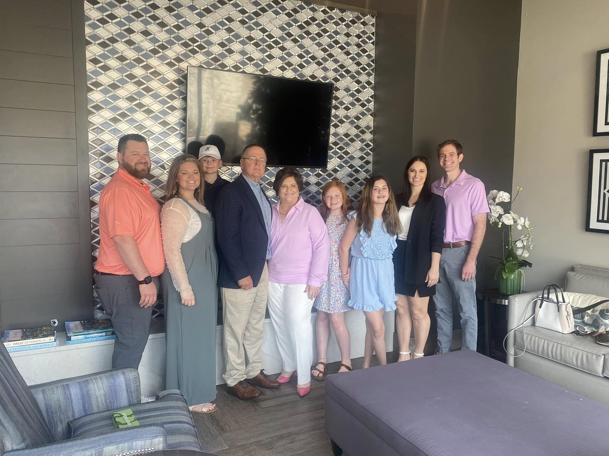 Group of ten people smiling at camera in modern living room with fireplace