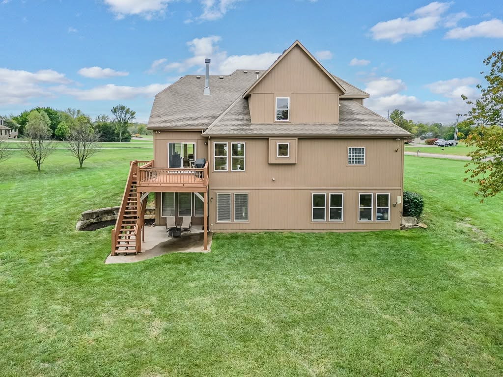 Two-story tan house with deck and manicured lawn in suburban setting