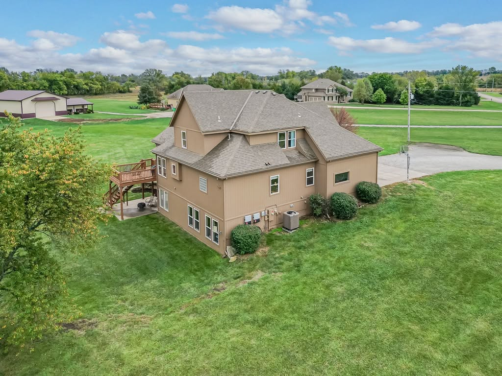 Tan two-story house with gray roof on large green lawn in rural area