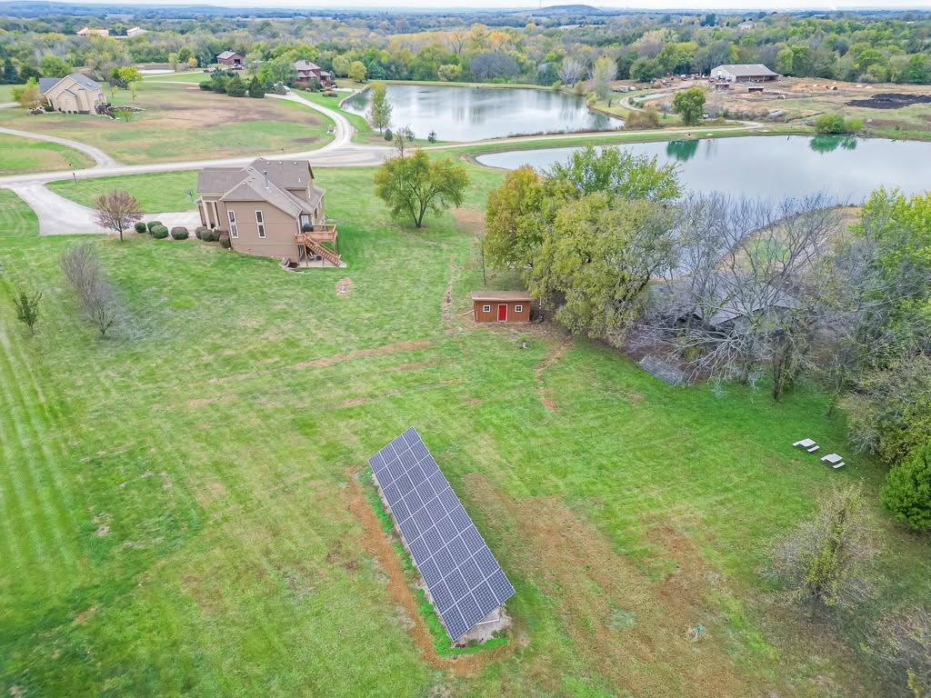 Aerial view of rural property with solar panels, house, pond, and barn