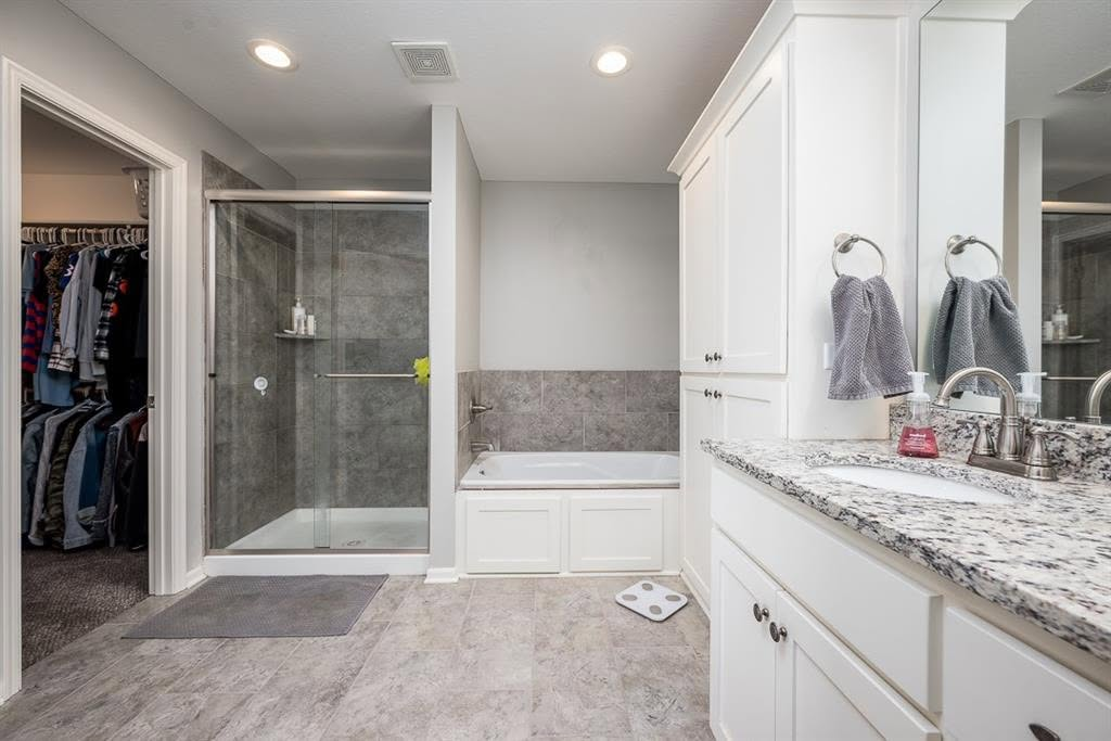 Modern luxury bathroom with white cabinetry, granite countertop, walk-in shower, and adjoining closet