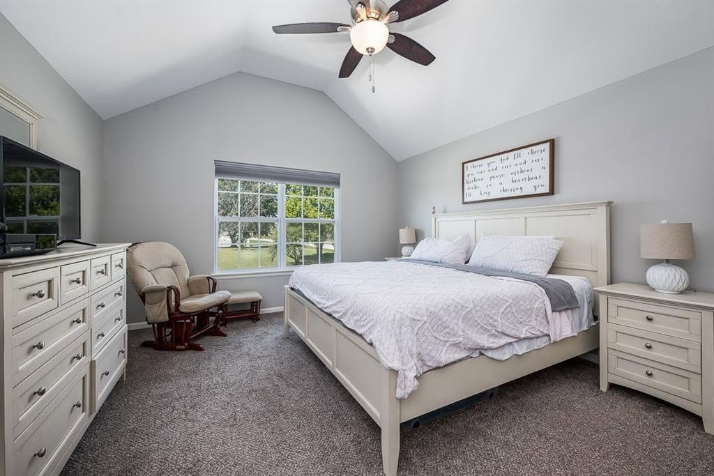 Spacious master bedroom with white furniture, vaulted ceiling, large windows, and ceiling fan