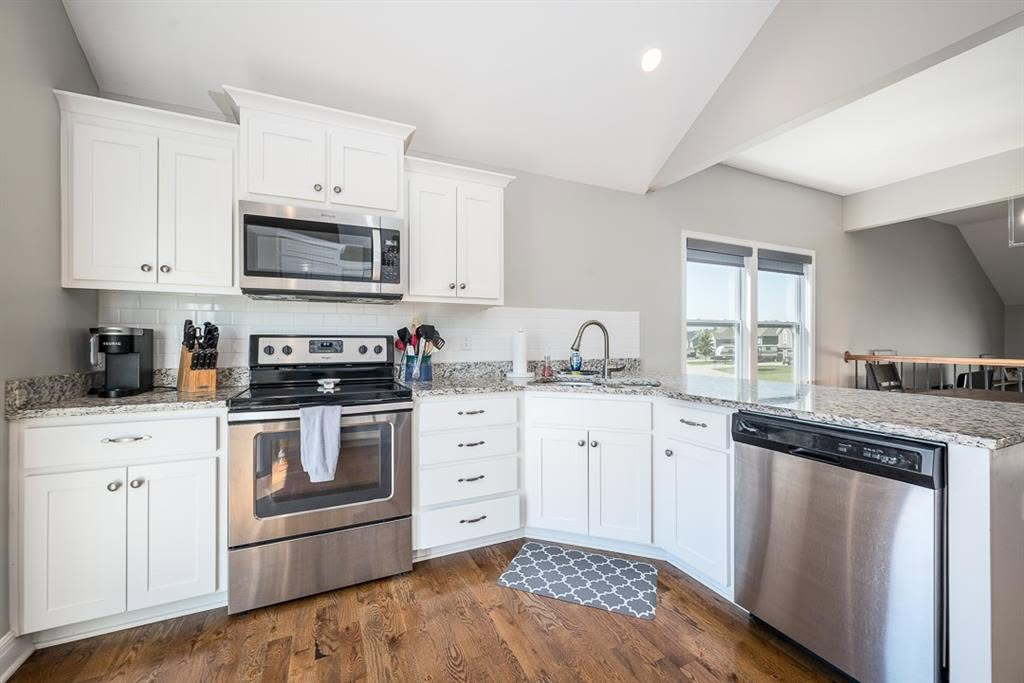 Modern kitchen with white cabinets, granite countertops, stainless steel appliances, and wood flooring