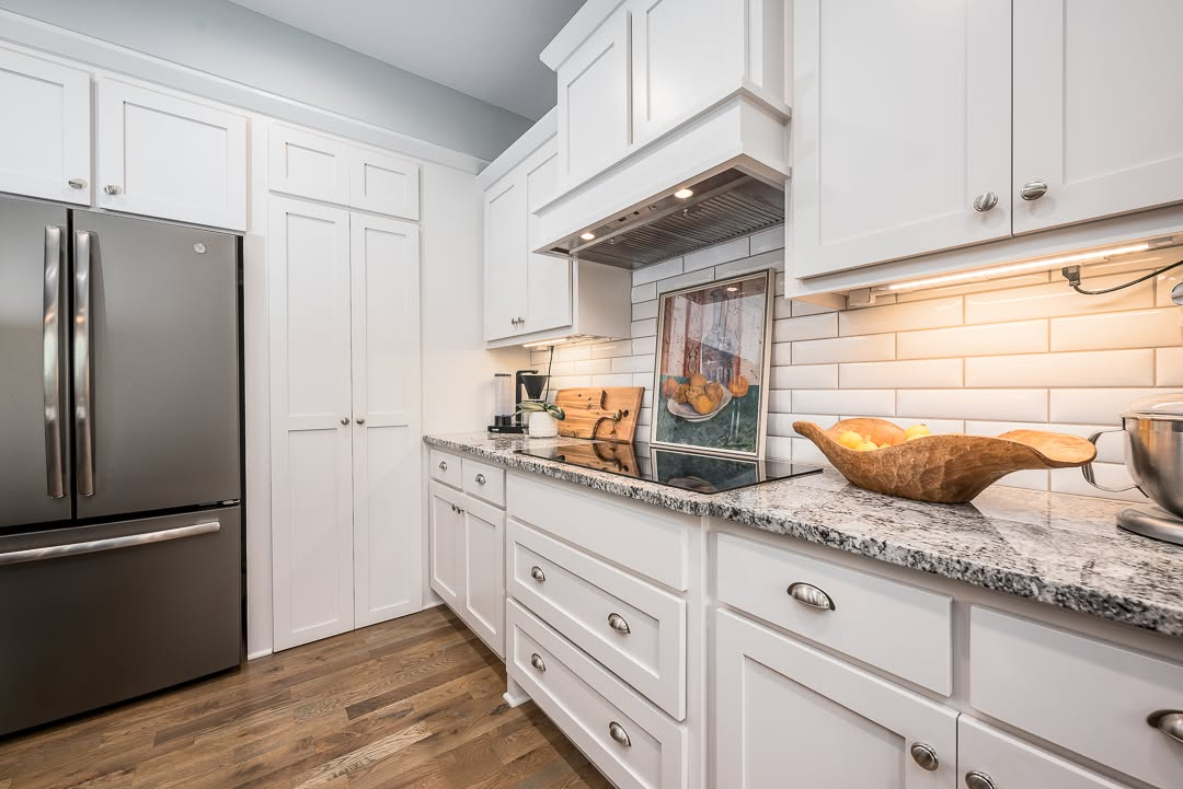 Modern white kitchen with granite countertops, stainless steel appliances, and subway tile backsplash