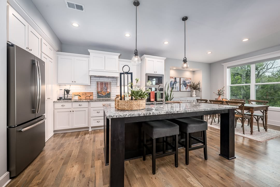 Modern kitchen with white cabinetry, black island, granite countertops, and stainless steel appliances