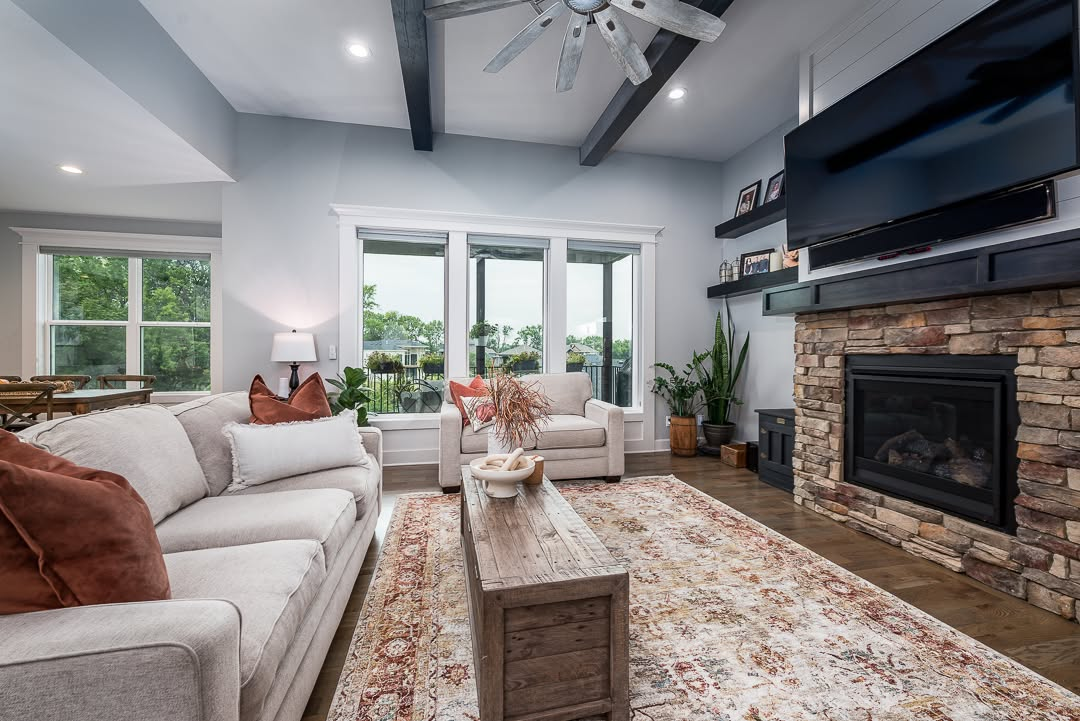 Modern living room with beige sofa, fireplace, wood beams, and view of green landscape through glass doors