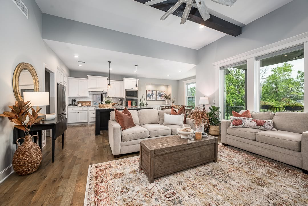 Modern open-concept living room with beige sofas, wooden coffee table, and kitchen visible in background
