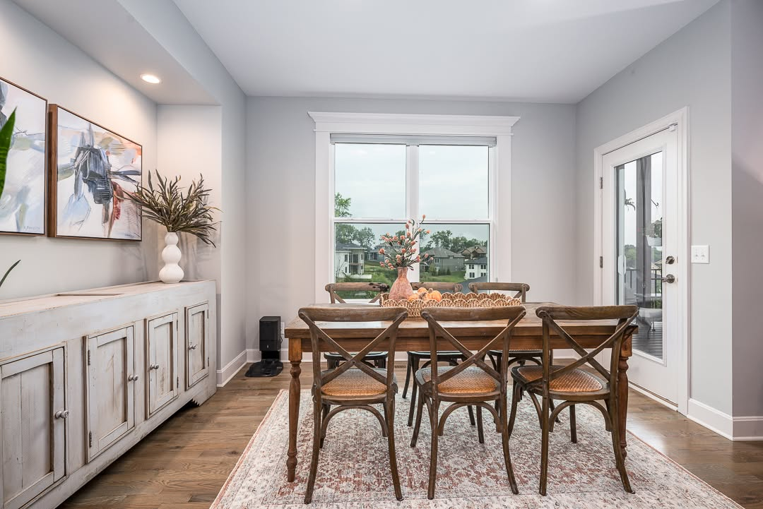 Modern dining room with wooden table, cross-back chairs, and large windows overlooking suburban landscape
