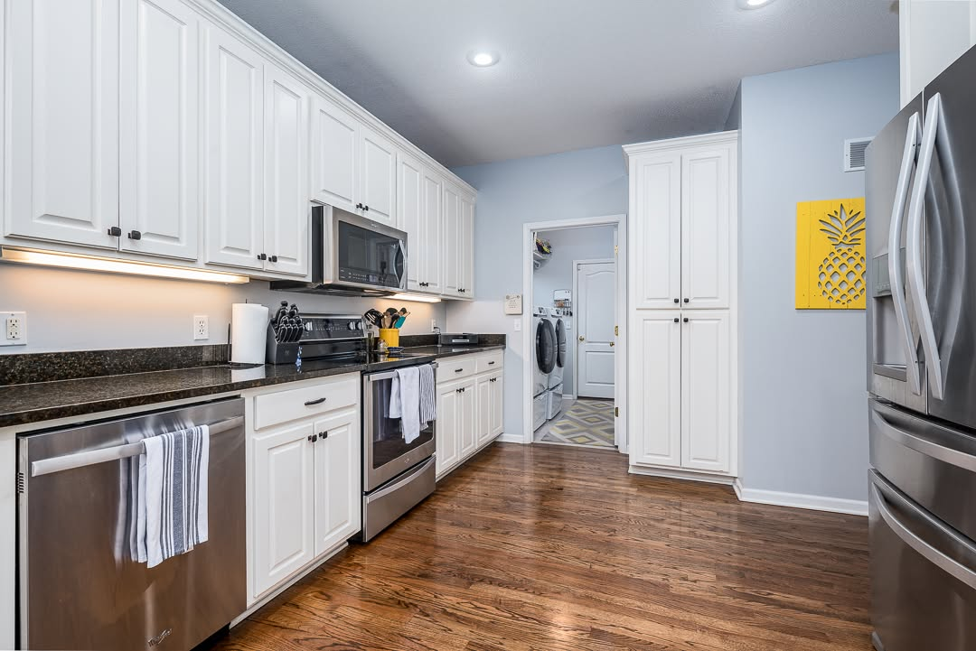 Modern kitchen with white cabinets, stainless steel appliances, dark countertops, and wood flooring