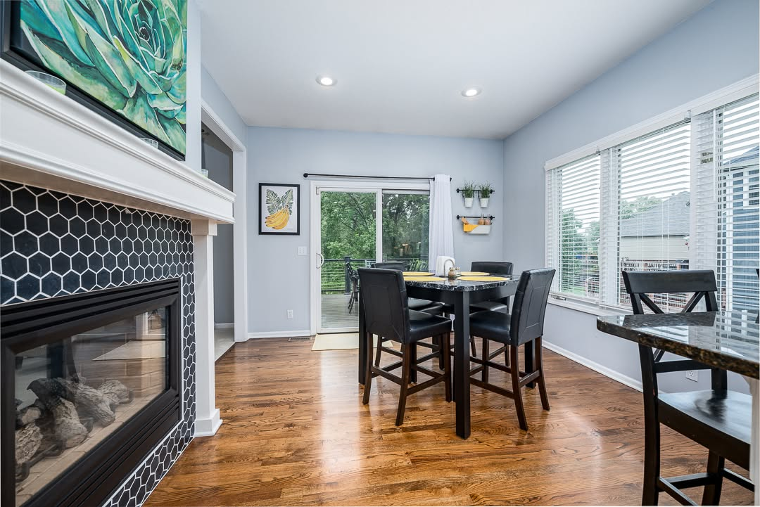 Modern dining room with fireplace, black hexagon backsplash, wood table, and glass doors overlooking deck