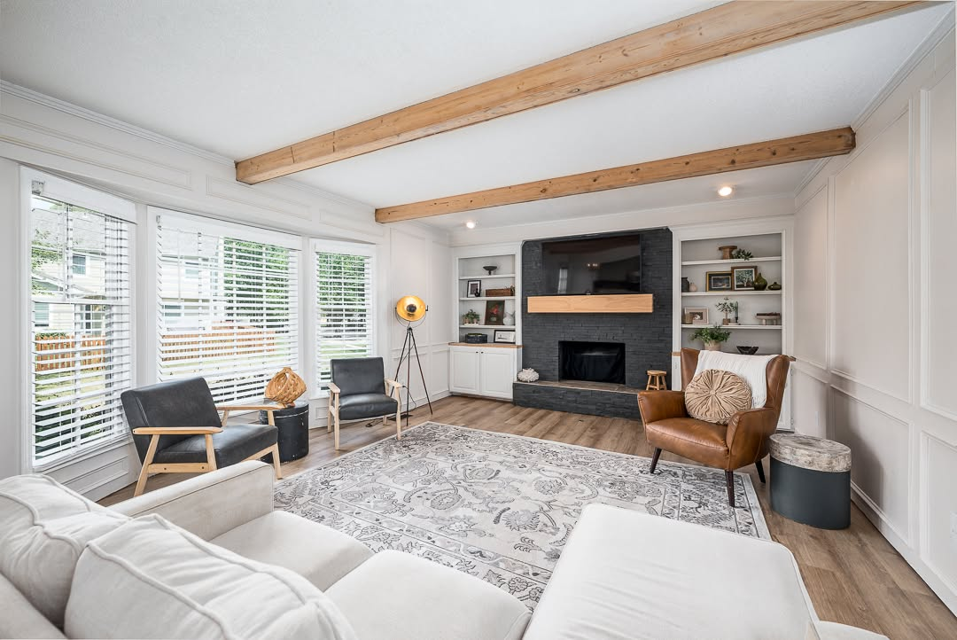 Modern living room with exposed wooden beams, fireplace, leather chairs, and large windows with shutters
