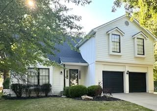 Two-story white house with black roof, two-car garage, and mature trees in front yard