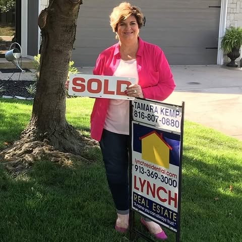 Real estate agent holding sold sign in front of house